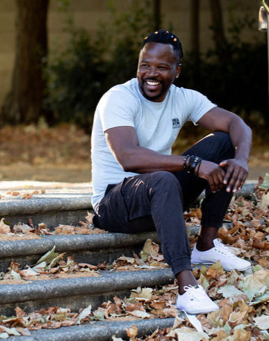 Man sitting on a metal railing with leaves on the ground wearing white Classic Taygras