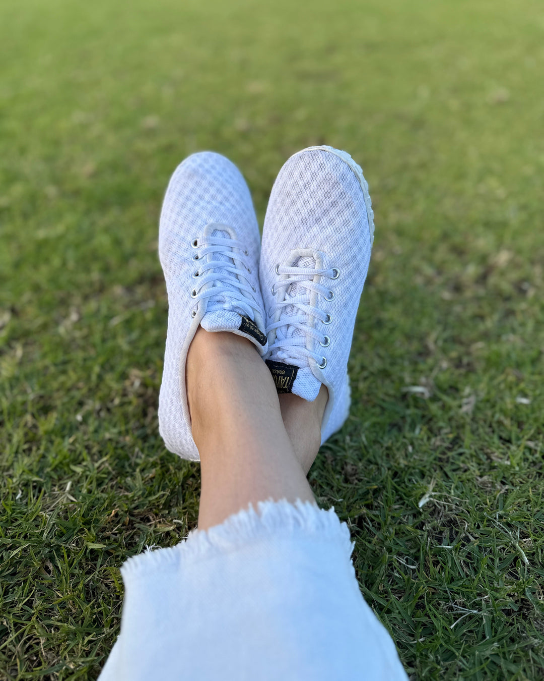 White Corrida sneakers on a person's feet with a grassy background